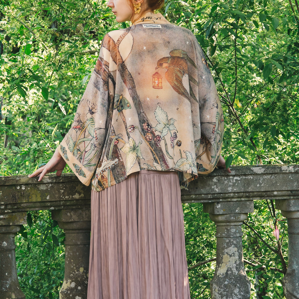 
                  
                    Model wearing an enchanting cropped kimono duster featuring illustrations by Charles van Sandwyck's, crafted from airy bamboo-based viscose with a touch of whimsical magic - Market of Stars
                  
                
