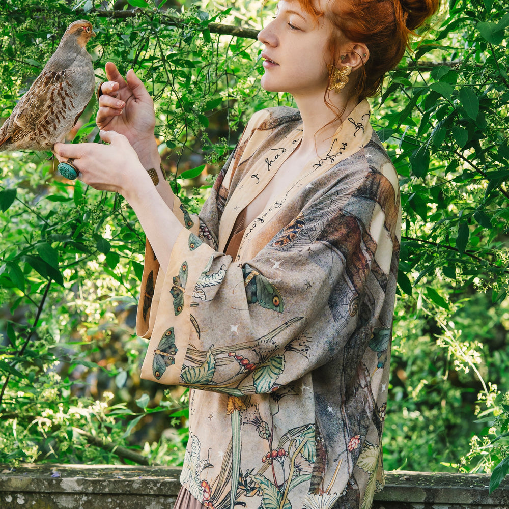 
                  
                    Model wearing an enchanting cropped kimono duster featuring illustrations by Charles van Sandwyck's, crafted from airy bamboo-based viscose with a touch of whimsical magic - Market of Stars
                  
                