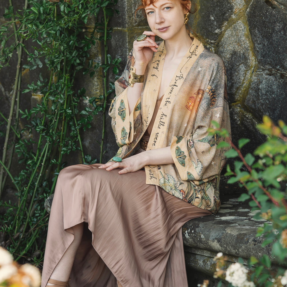 
                  
                    Model wearing an enchanting cropped kimono duster featuring illustrations by Charles van Sandwyck's, crafted from airy bamboo-based viscose with a touch of whimsical magic - Market of Stars
                  
                