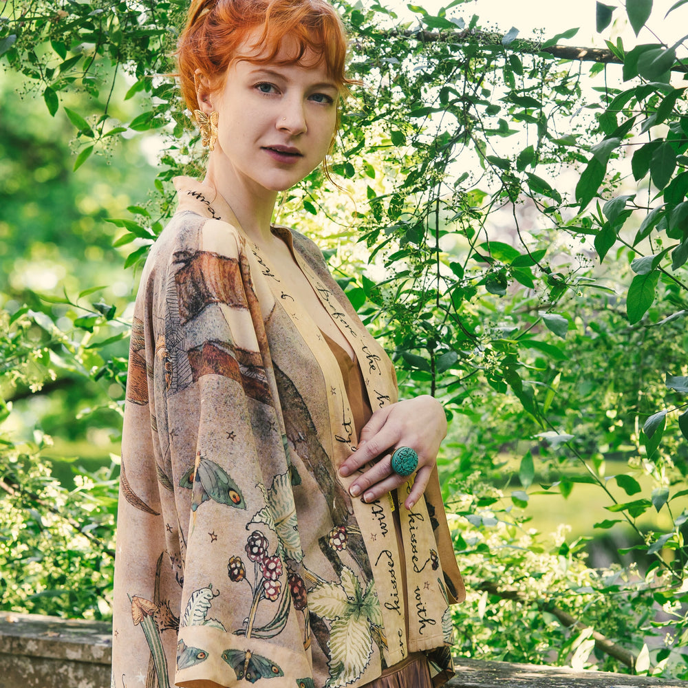 
                  
                    Model wearing an enchanting cropped kimono duster featuring illustrations by Charles van Sandwyck's, crafted from airy bamboo-based viscose with a touch of whimsical magic - Market of Stars
                  
                