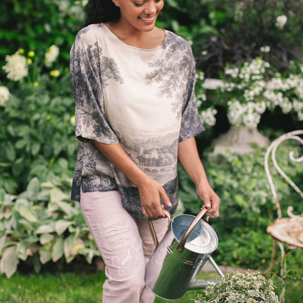 
                  
                    Model wearing the Still I Rise Luxe Tee with wide scoop neck and soft bamboo-based viscose, featuring vintage landscape etching and an inspiring message – Market of Stars
                  
                