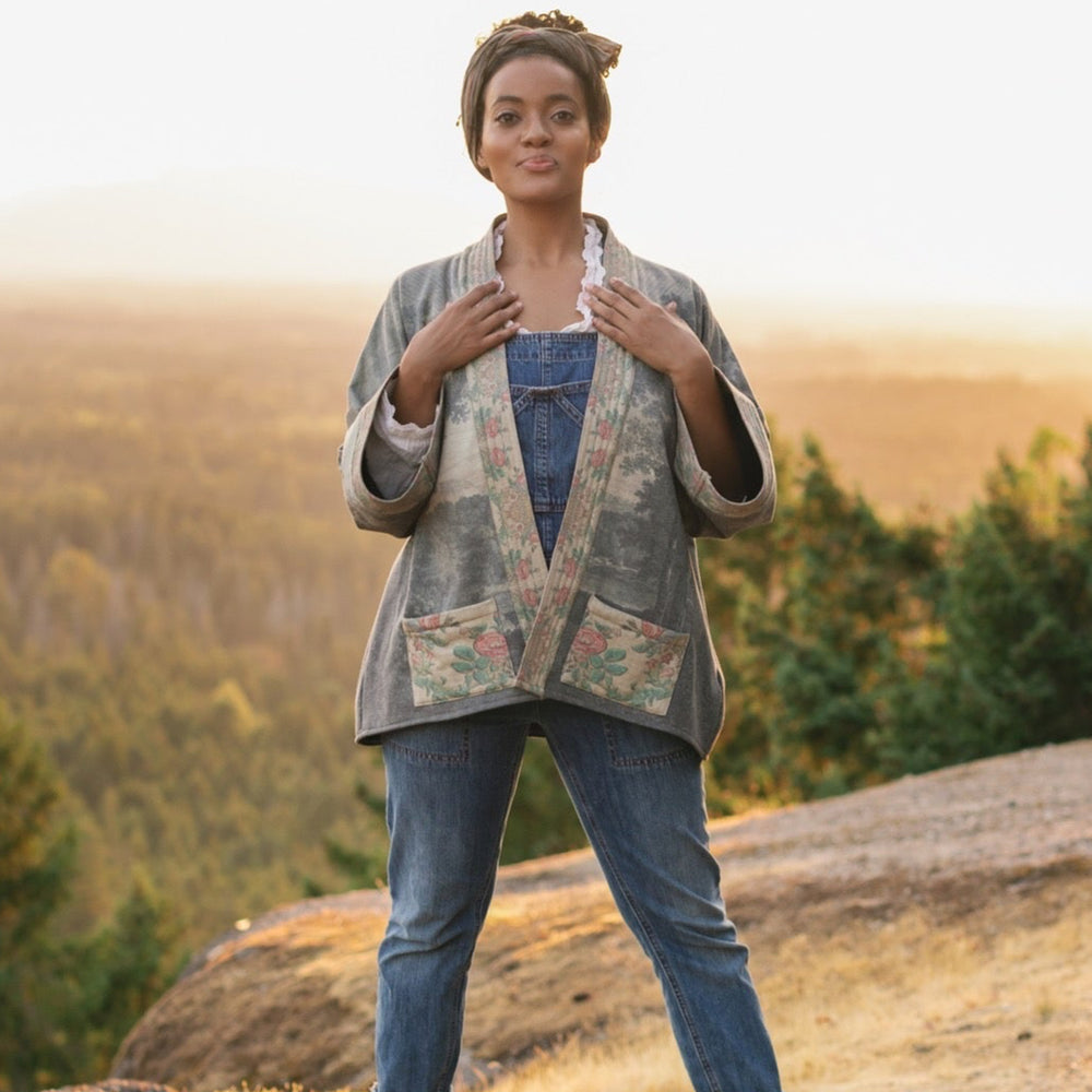 
                  
                    Model wearing the Still I Rise Cottage Cardigan featuring a soft fleece lining and antique landscape etchings in a design inspired by rising strength – Market of Stars
                  
                