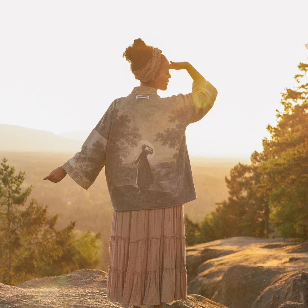 
                  
                    Model wearing the Still I Rise Cottage Cardigan featuring a soft fleece lining and antique landscape etchings in a design inspired by rising strength – Market of Stars
                  
                