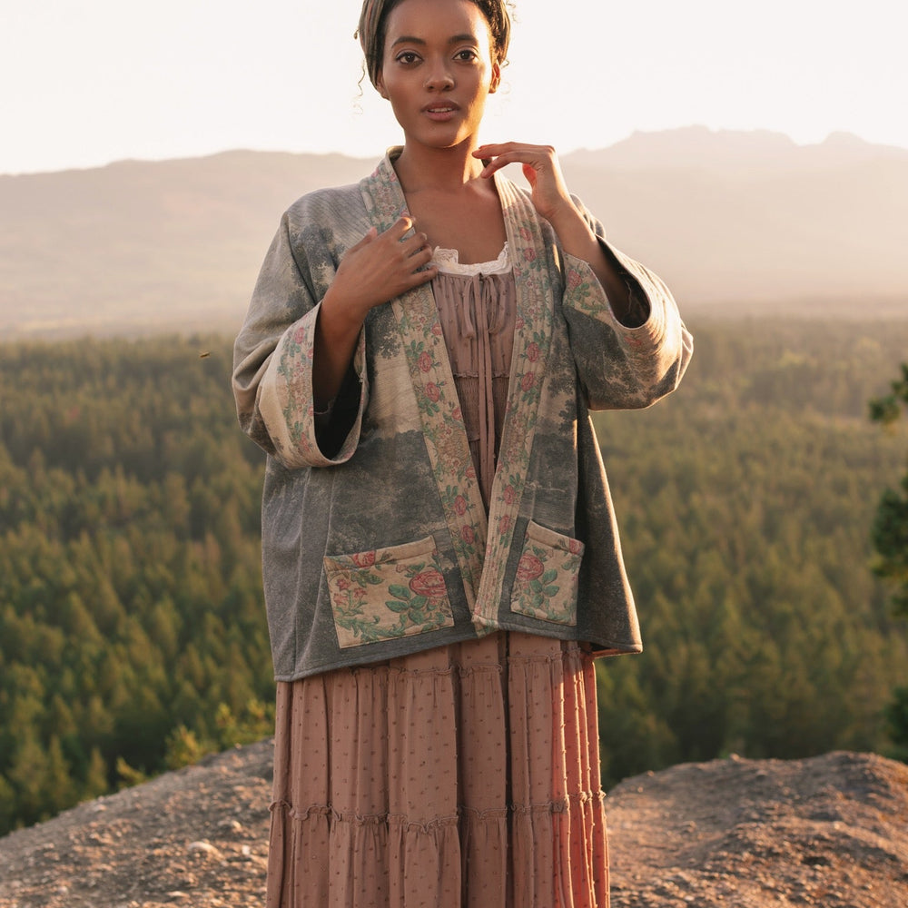 
                  
                    Model wearing the Still I Rise Cottage Cardigan featuring a soft fleece lining and antique landscape etchings in a design inspired by rising strength – Market of Stars
                  
                
