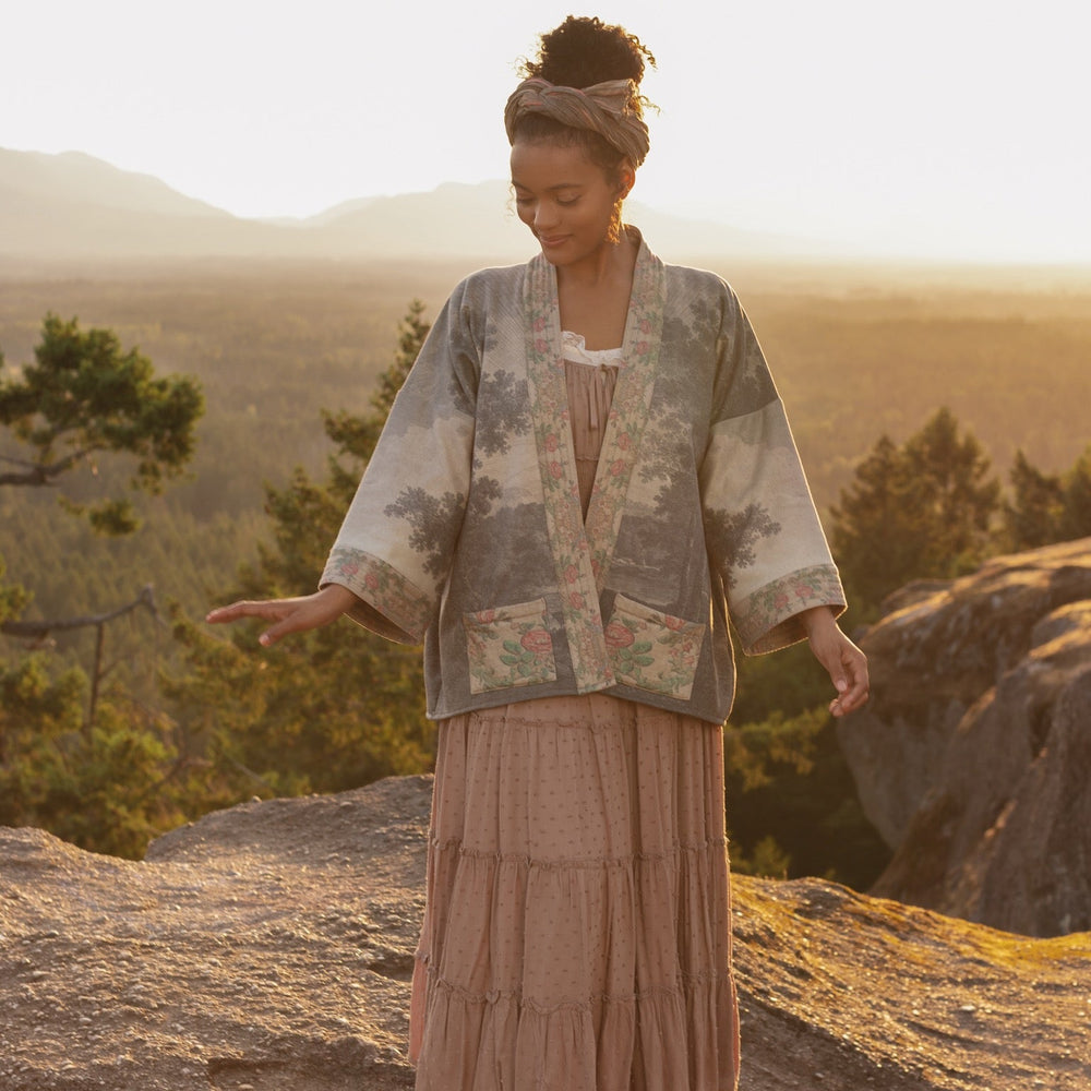 
                  
                    Model wearing the Still I Rise Cottage Cardigan featuring a soft fleece lining and antique landscape etchings in a design inspired by rising strength – Market of Stars
                  
                