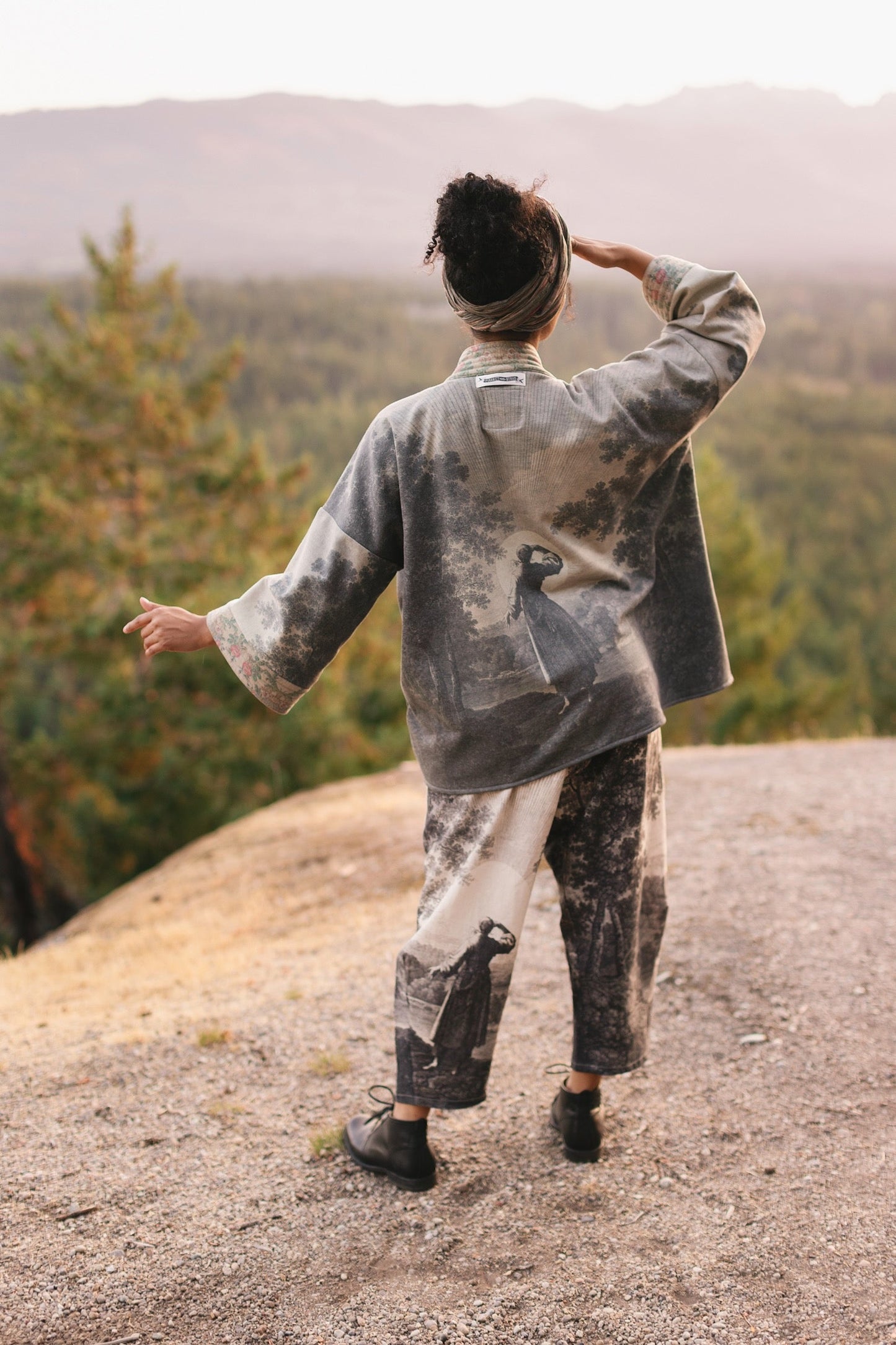 Model wearing the Still I Rise Cottage Cardigan featuring a soft fleece lining and antique landscape etchings in a design inspired by rising strength – Market of Stars