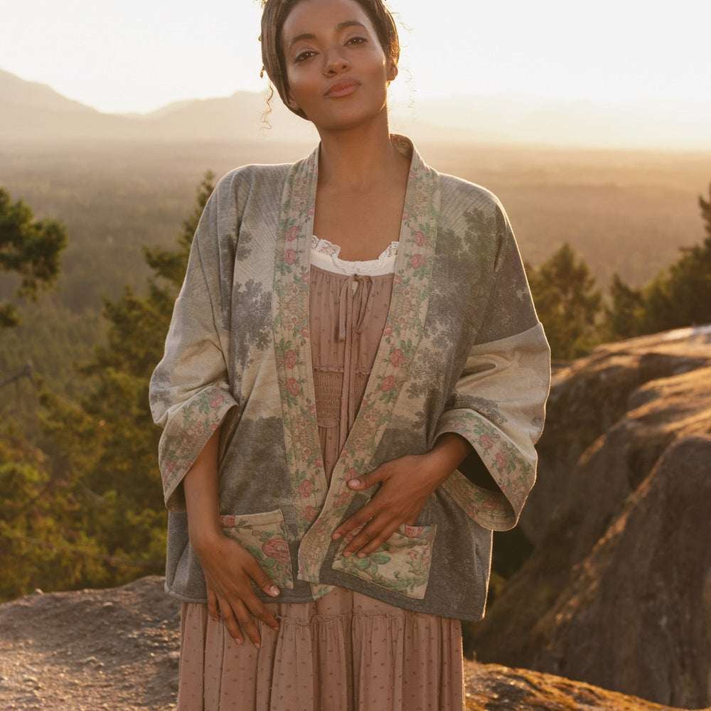 
                  
                    Model wearing the Still I Rise Cottage Cardigan featuring a soft fleece lining and antique landscape etchings in a design inspired by rising strength – Market of Stars
                  
                