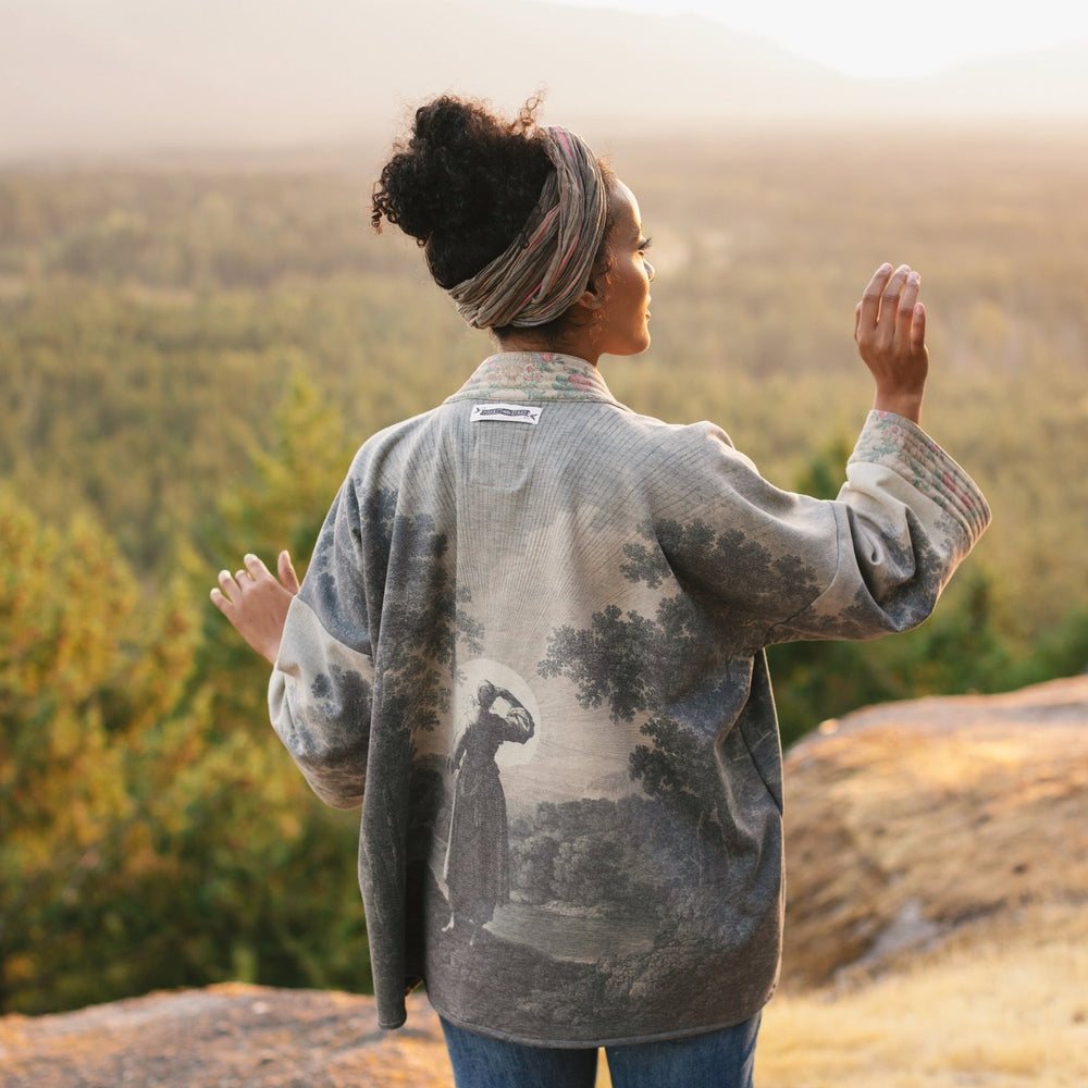 
                  
                    Model wearing the Still I Rise Cottage Cardigan featuring a soft fleece lining and antique landscape etchings in a design inspired by rising strength – Market of Stars
                  
                