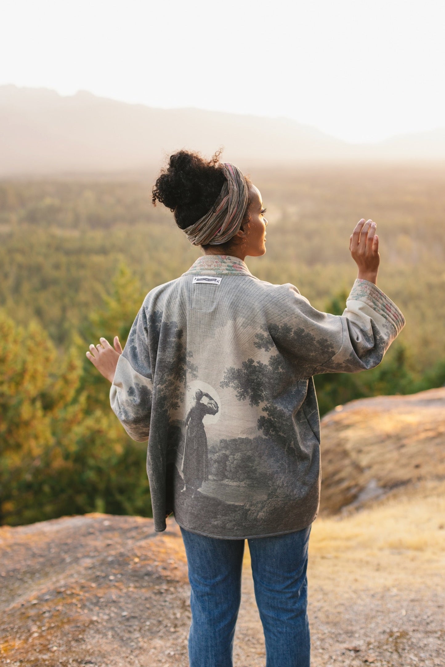 Model wearing the Still I Rise Cottage Cardigan featuring a soft fleece lining and antique landscape etchings in a design inspired by rising strength – Market of Stars