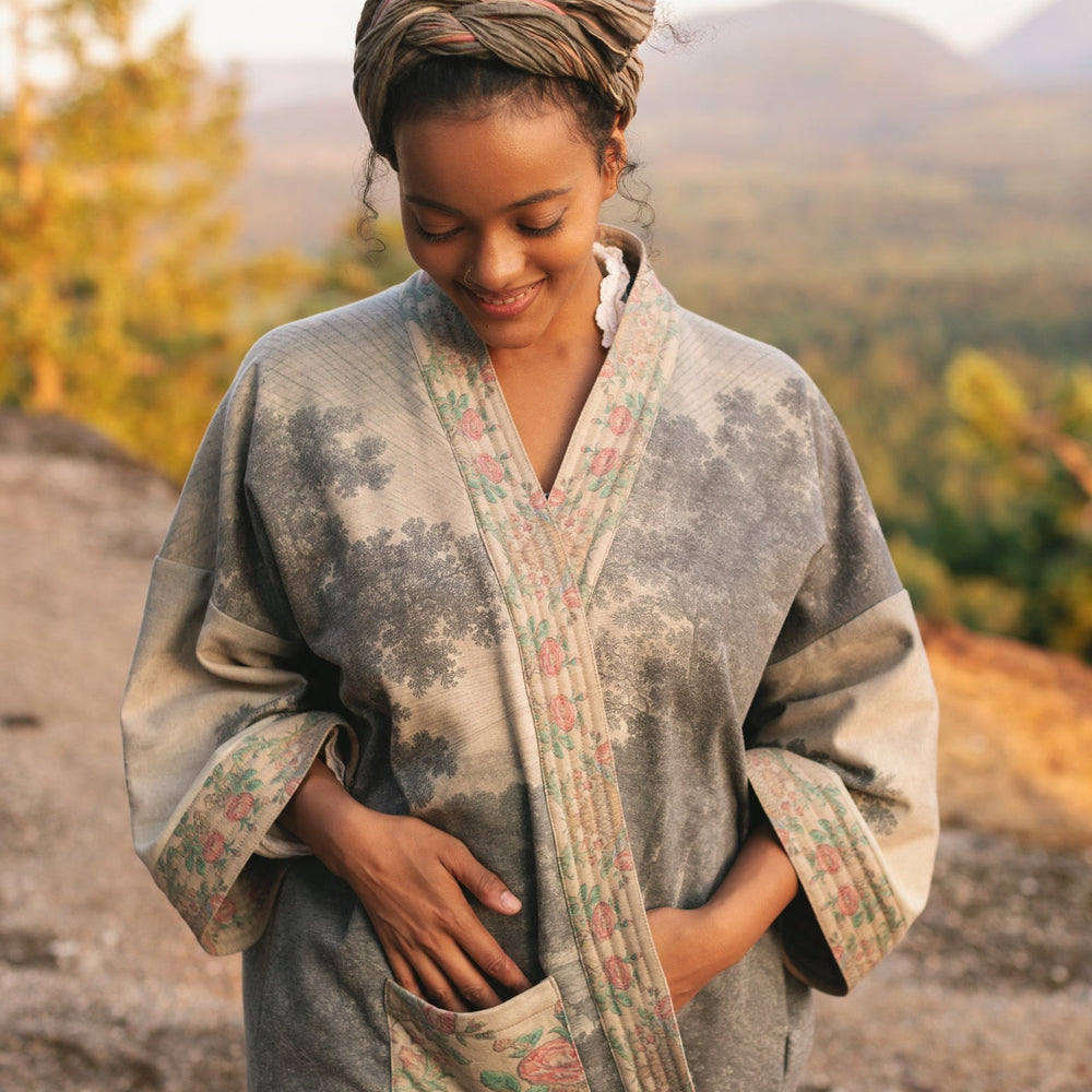 
                  
                    Model wearing the Still I Rise Cottage Cardigan featuring a soft fleece lining and antique landscape etchings in a design inspired by rising strength – Market of Stars
                  
                