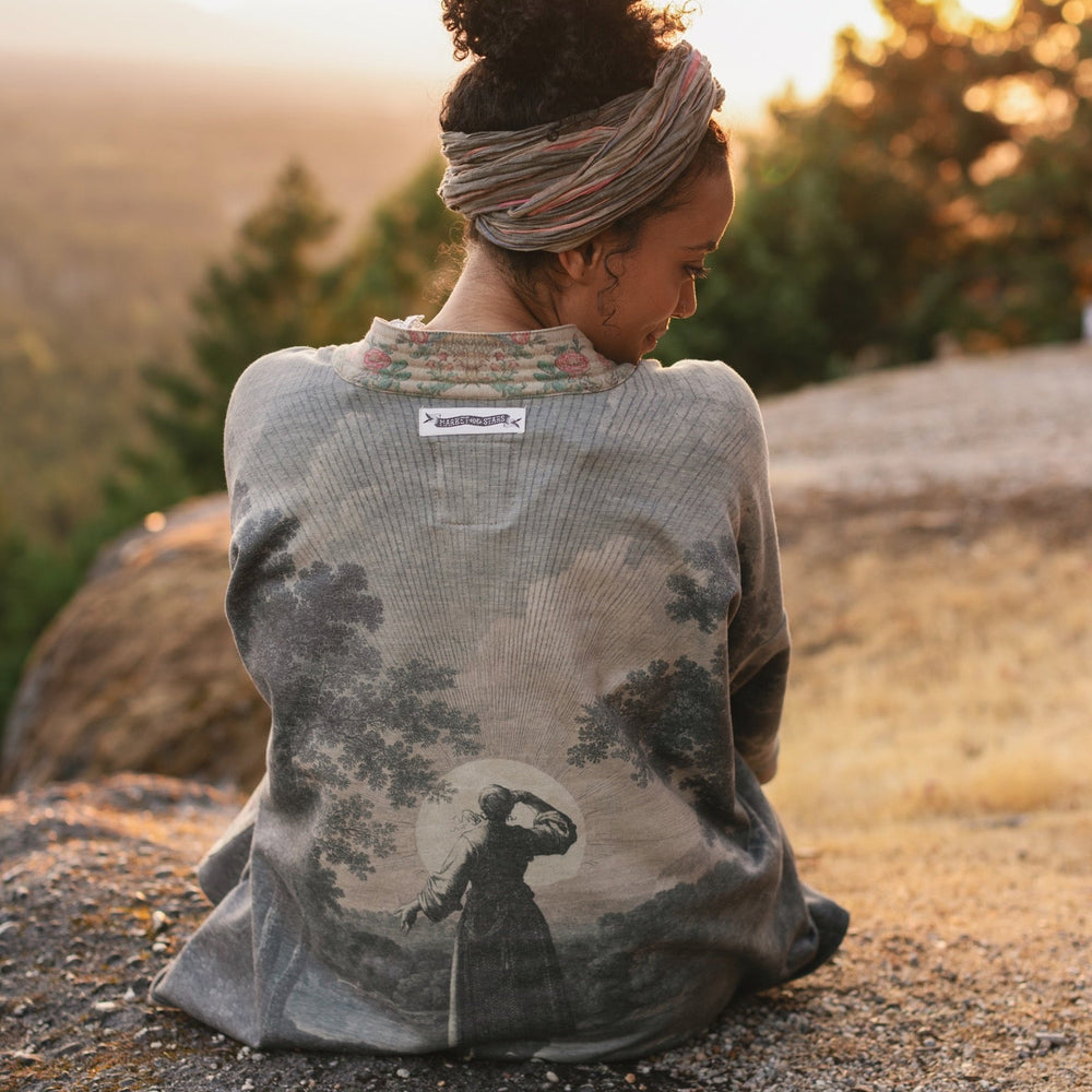 
                  
                    Model wearing the Still I Rise Cottage Cardigan featuring a soft fleece lining and antique landscape etchings in a design inspired by rising strength – Market of Stars
                  
                