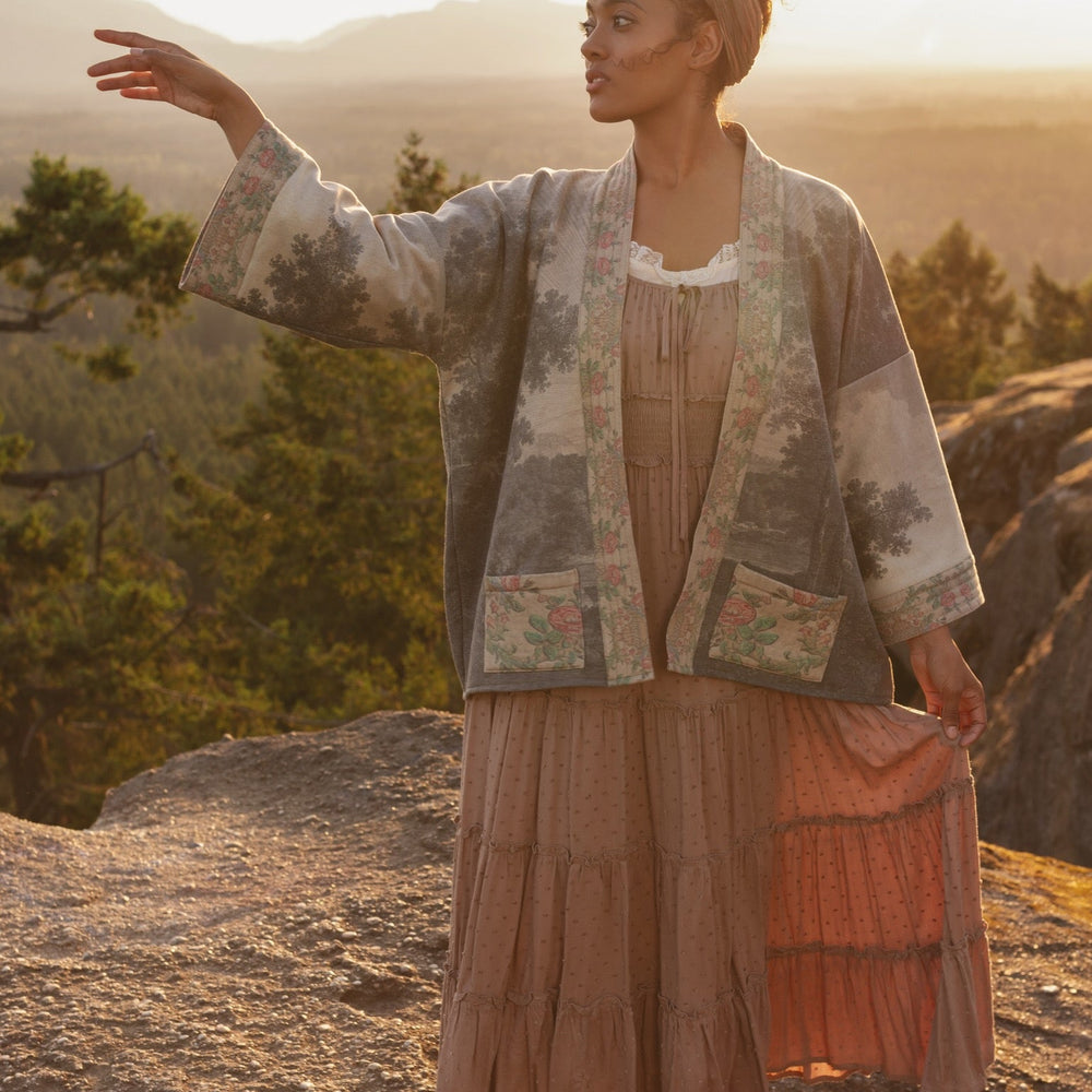 
                  
                    Model wearing the Still I Rise Cottage Cardigan featuring a soft fleece lining and antique landscape etchings in a design inspired by rising strength – Market of Stars
                  
                