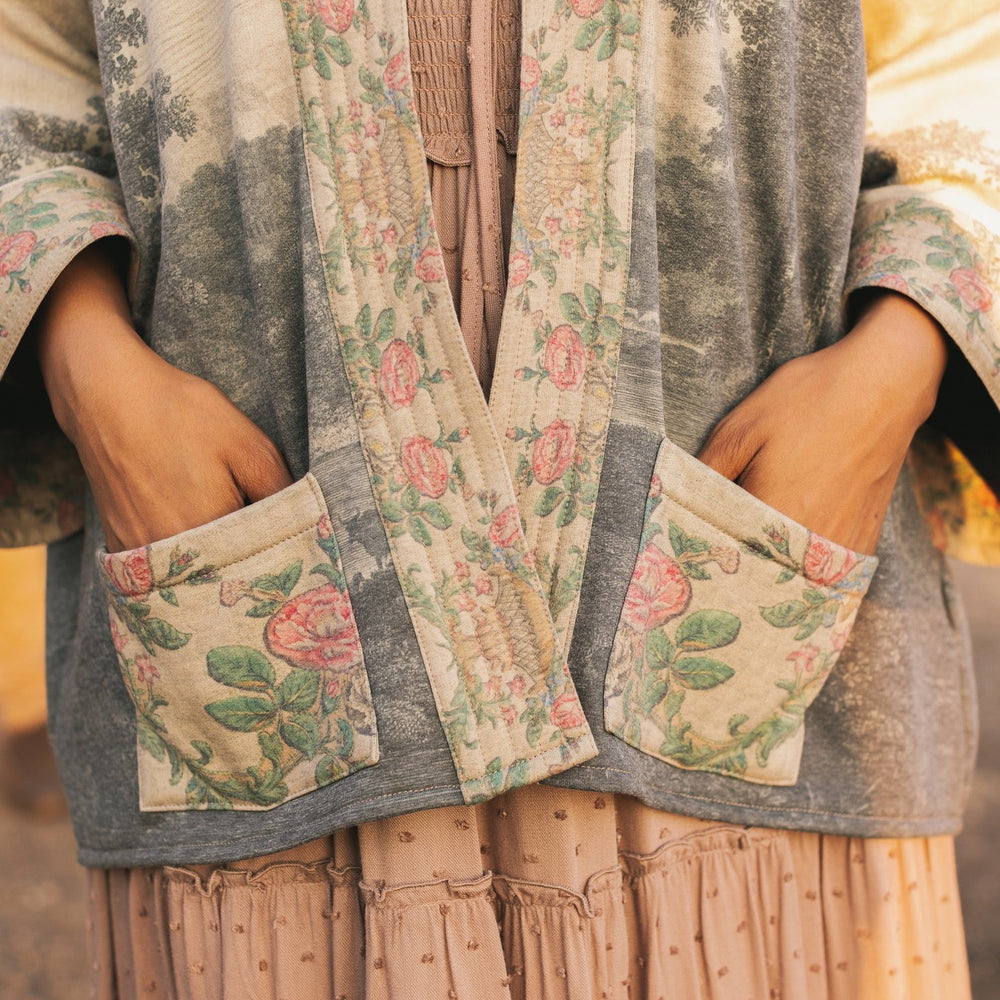 
                  
                    Model wearing the Still I Rise Cottage Cardigan featuring a soft fleece lining and antique landscape etchings in a design inspired by rising strength – Market of Stars
                  
                