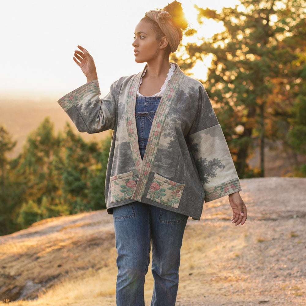 
                  
                    Model wearing the Still I Rise Cottage Cardigan featuring a soft fleece lining and antique landscape etchings in a design inspired by rising strength – Market of Stars
                  
                