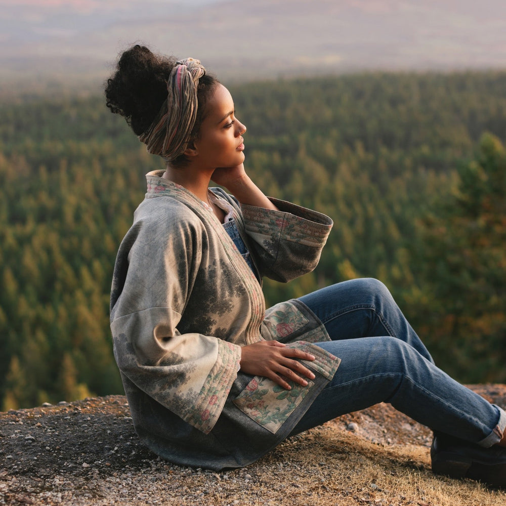 
                  
                    Model wearing the Still I Rise Cottage Cardigan featuring a soft fleece lining and antique landscape etchings in a design inspired by rising strength – Market of Stars
                  
                