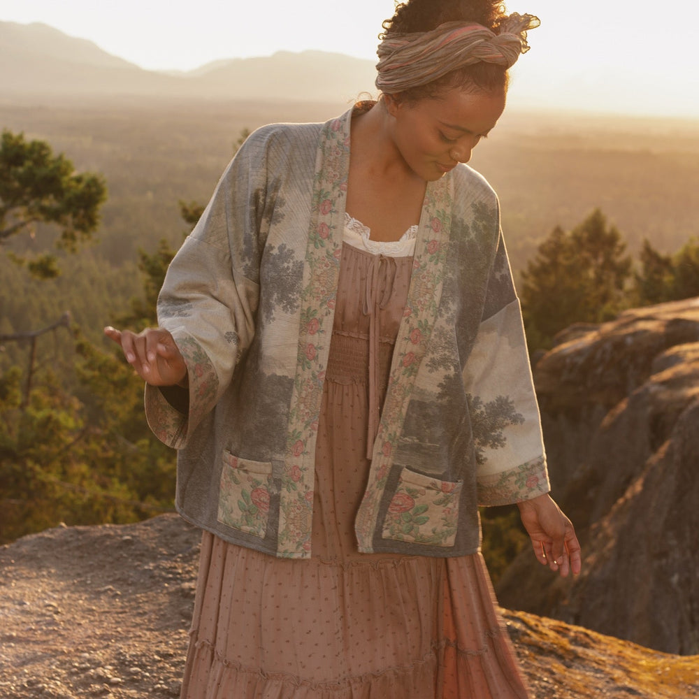 
                  
                    Model wearing the Still I Rise Cottage Cardigan featuring a soft fleece lining and antique landscape etchings in a design inspired by rising strength – Market of Stars
                  
                