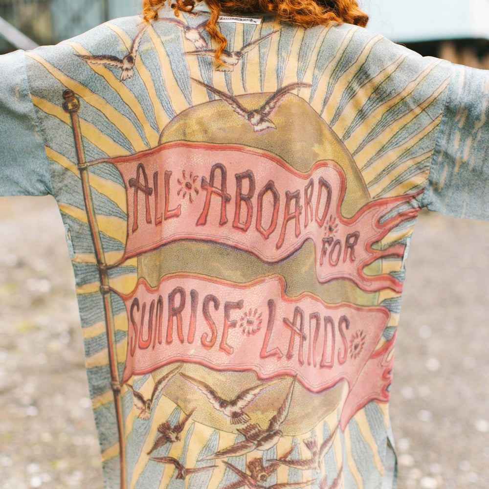 
                  
                    Lightweight duster featuring antique sunrise sky, mermaid, shell, and soaring birds artwork, shown on model at the beach – Market of Stars
                  
                