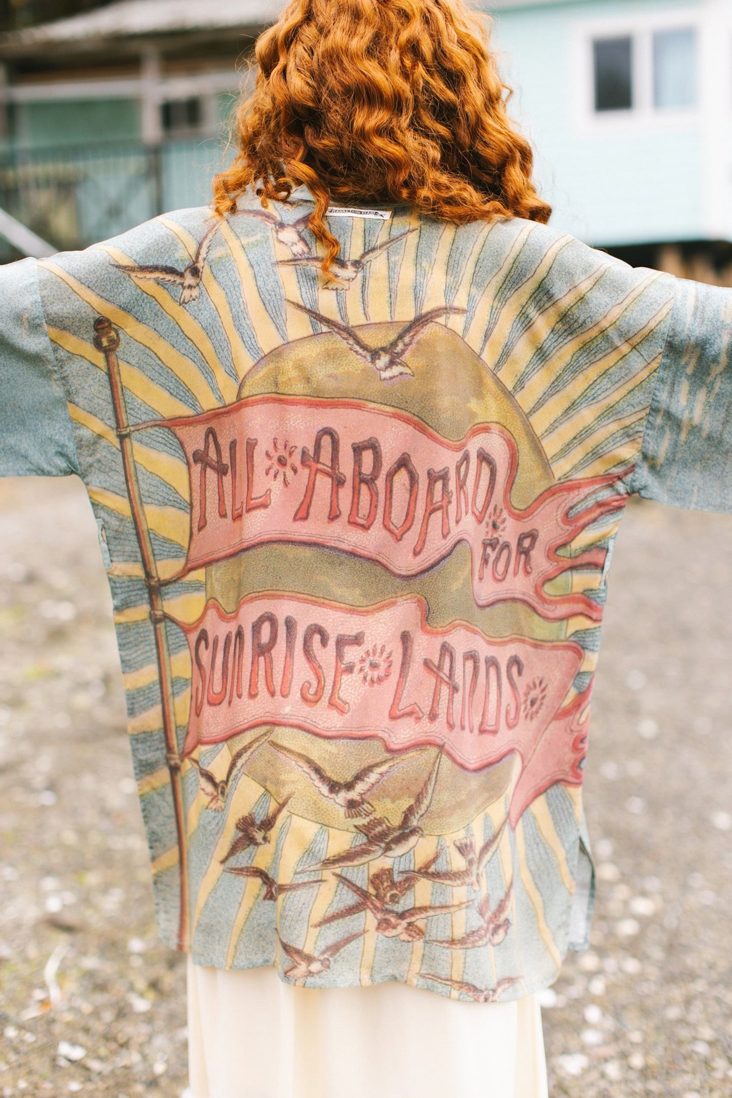 Lightweight duster featuring antique sunrise sky, mermaid, shell, and soaring birds artwork, shown on model at the beach – Market of Stars