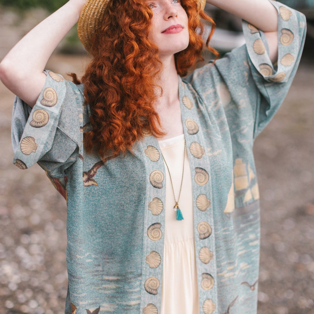 
                  
                    Lightweight duster featuring antique sunrise sky, mermaid, shell, and soaring birds artwork, shown on model at the beach – Market of Stars
                  
                
