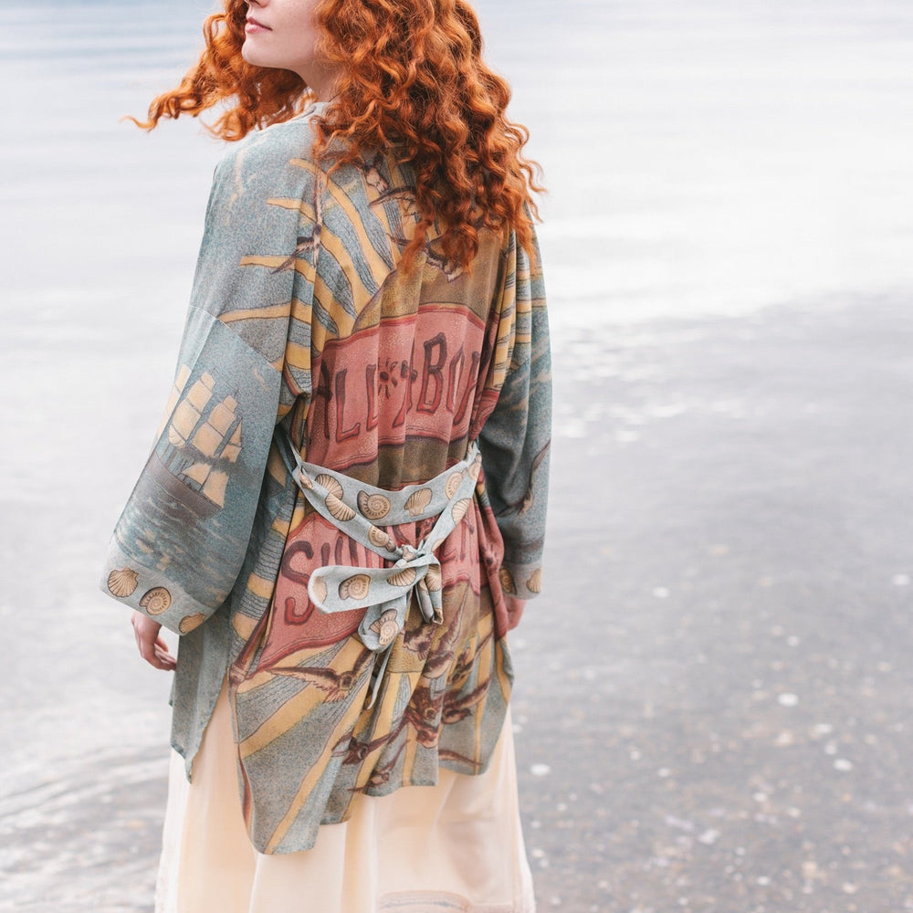 
                  
                    Lightweight duster featuring antique sunrise sky, mermaid, shell, and soaring birds artwork, shown on model at the beach – Market of Stars
                  
                