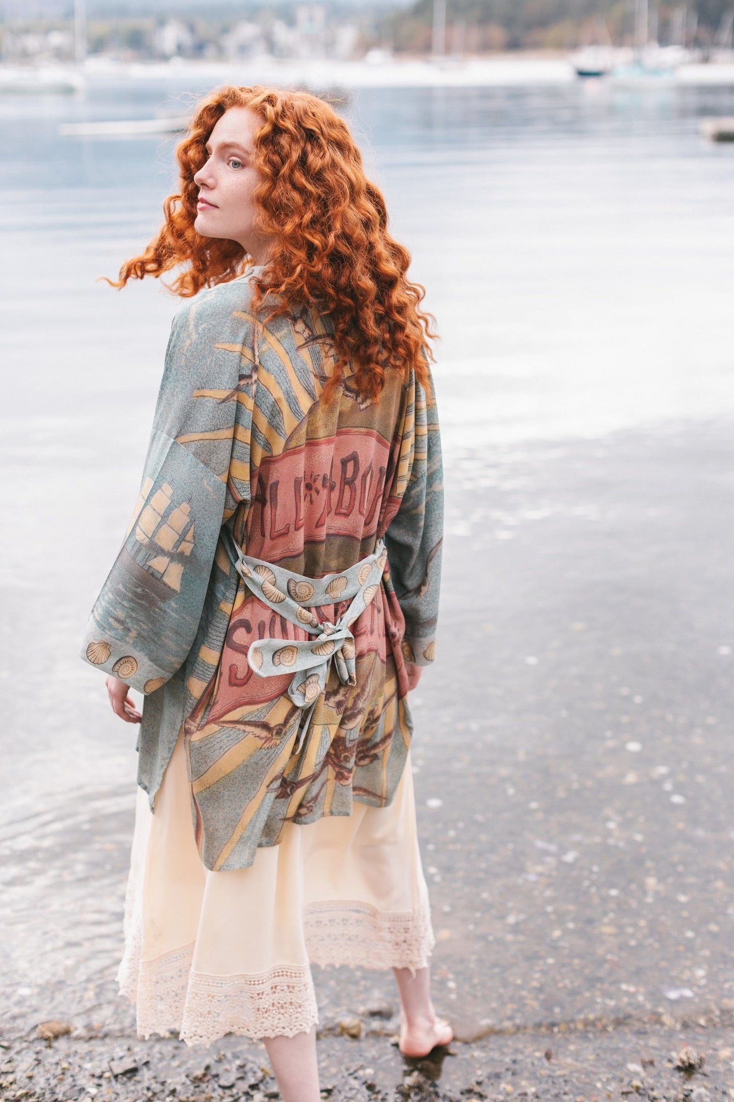 Lightweight duster featuring antique sunrise sky, mermaid, shell, and soaring birds artwork, shown on model at the beach – Market of Stars