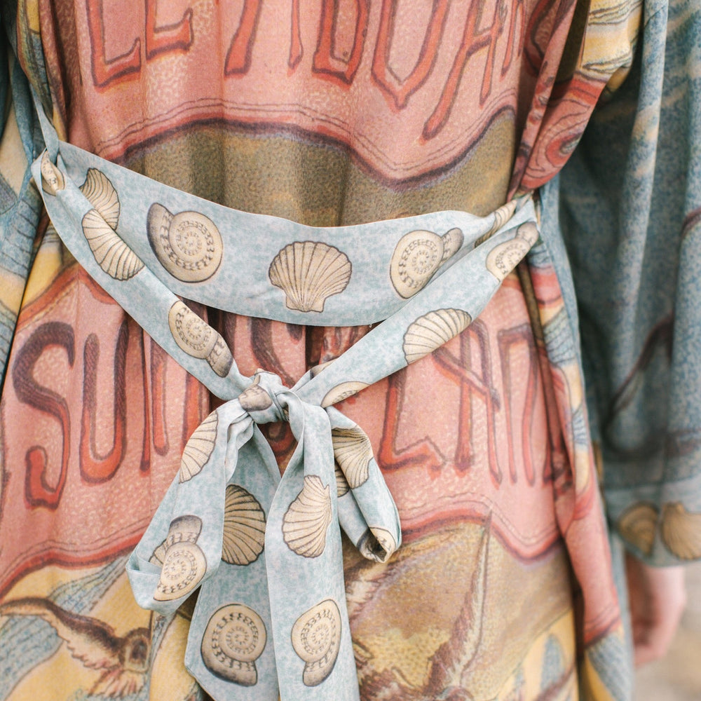 
                  
                    Lightweight duster featuring antique sunrise sky, mermaid, shell, and soaring birds artwork, shown on model at the beach – Market of Stars
                  
                