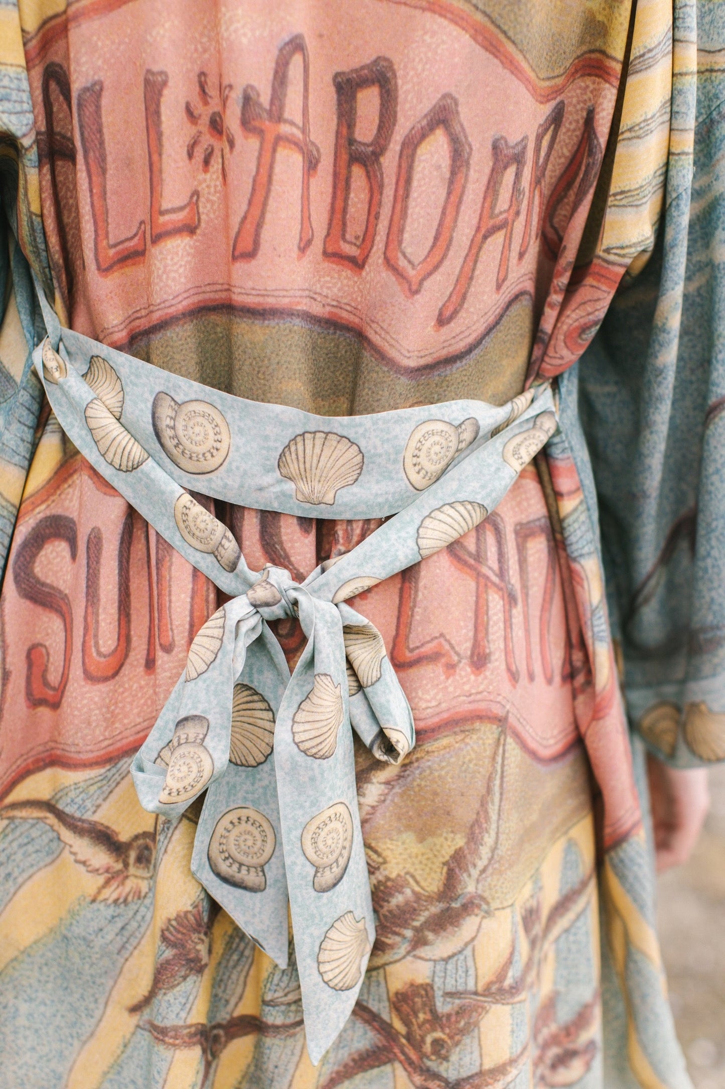 Lightweight duster featuring antique sunrise sky, mermaid, shell, and soaring birds artwork, shown on model at the beach – Market of Stars