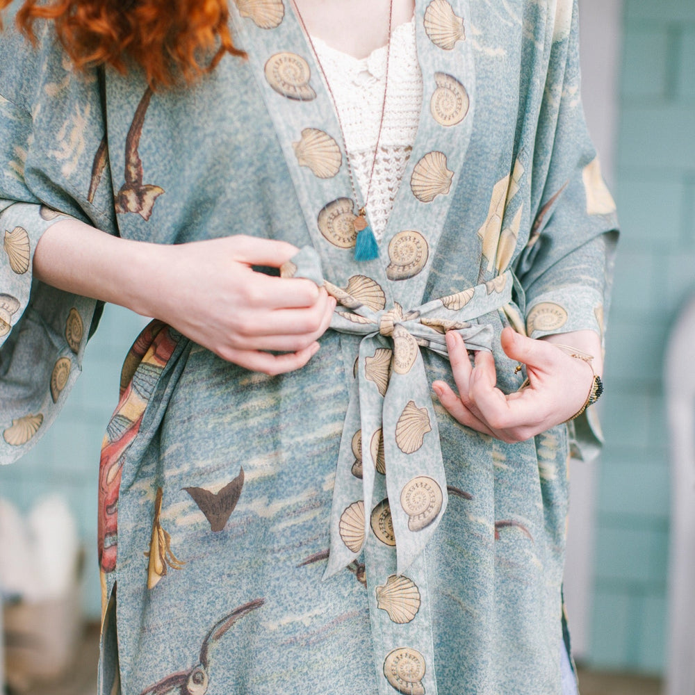 
                  
                    Lightweight duster featuring antique sunrise sky, mermaid, shell, and soaring birds artwork, shown on model at the beach – Market of Stars
                  
                
