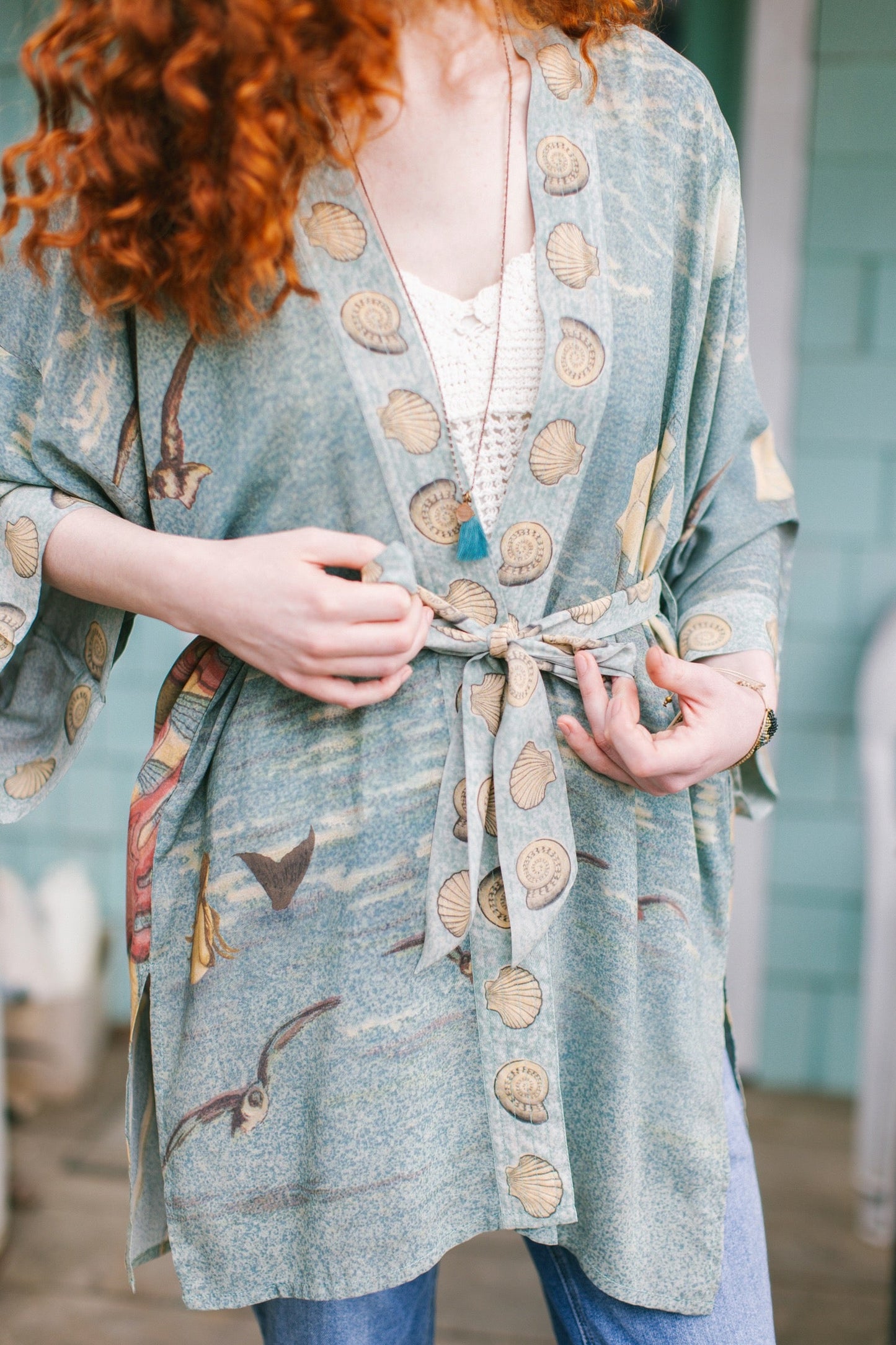 Lightweight duster featuring antique sunrise sky, mermaid, shell, and soaring birds artwork, shown on model at the beach – Market of Stars