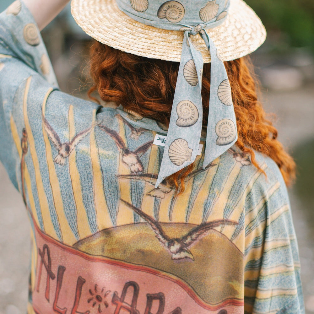 
                  
                    Lightweight duster featuring antique sunrise sky, mermaid, shell, and soaring birds artwork, shown on model at the beach – Market of Stars
                  
                