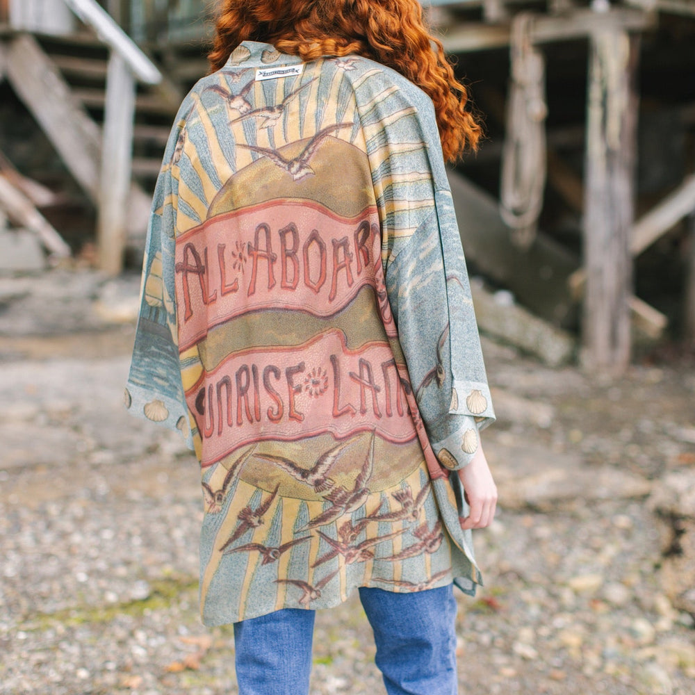
                  
                    Lightweight duster featuring antique sunrise sky, mermaid, shell, and soaring birds artwork, shown on model at the beach – Market of Stars
                  
                