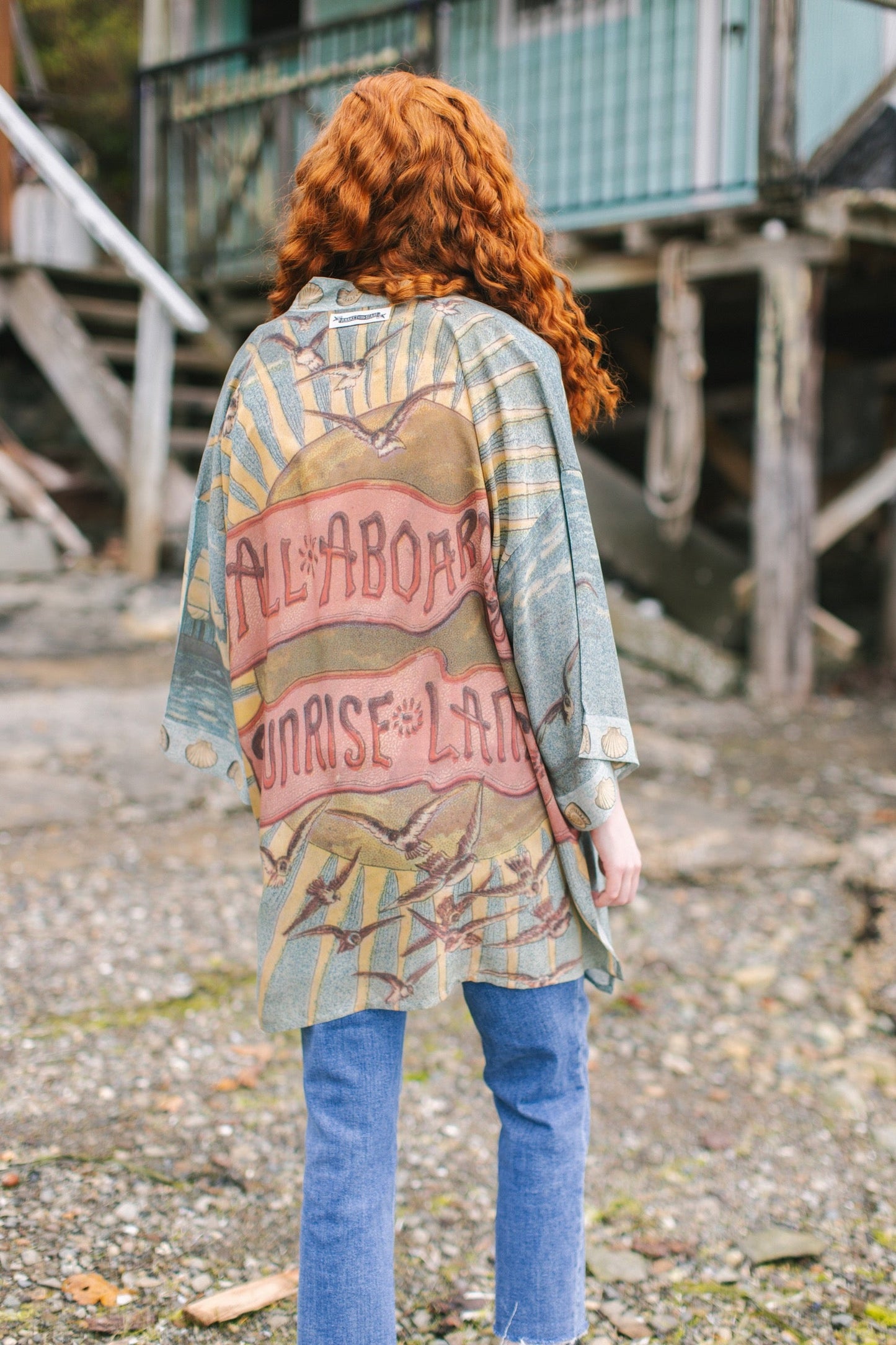 Lightweight duster featuring antique sunrise sky, mermaid, shell, and soaring birds artwork, shown on model at the beach – Market of Stars
