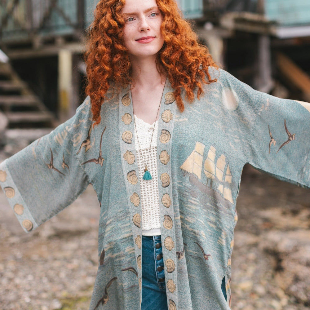 
                  
                    Lightweight duster featuring antique sunrise sky, mermaid, shell, and soaring birds artwork, shown on model at the beach – Market of Stars
                  
                