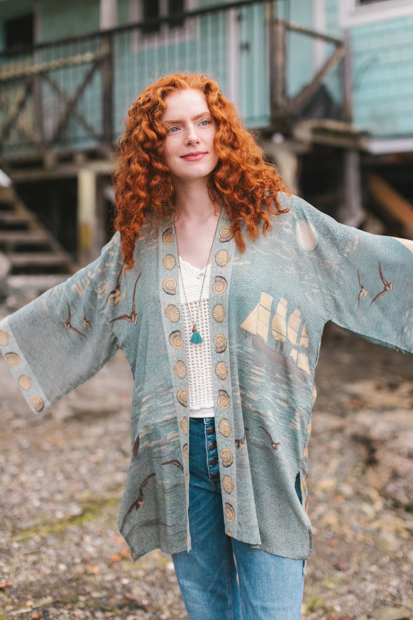 Lightweight duster featuring antique sunrise sky, mermaid, shell, and soaring birds artwork, shown on model at the beach – Market of Stars