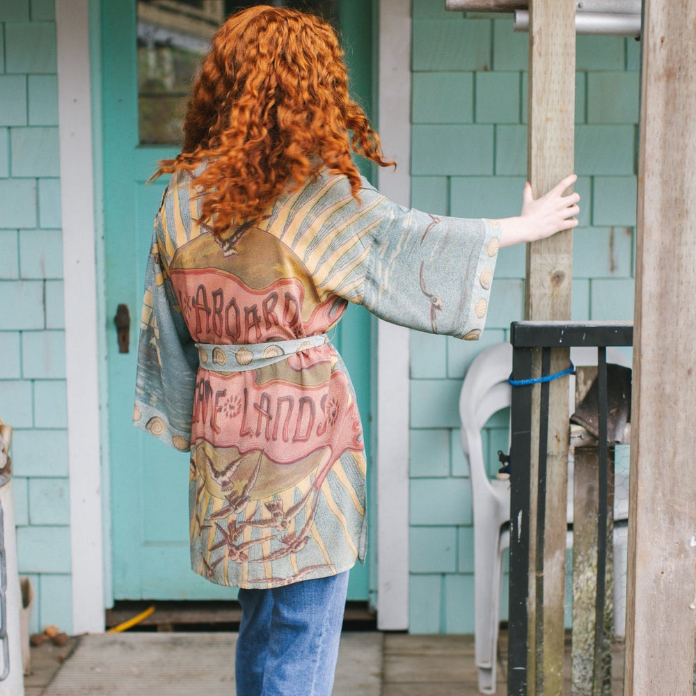 
                  
                    Lightweight duster featuring antique sunrise sky, mermaid, shell, and soaring birds artwork, shown on model at the beach – Market of Stars
                  
                