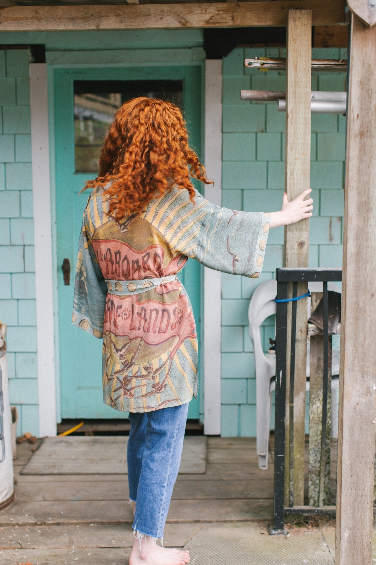 Lightweight duster featuring antique sunrise sky, mermaid, shell, and soaring birds artwork, shown on model at the beach – Market of Stars