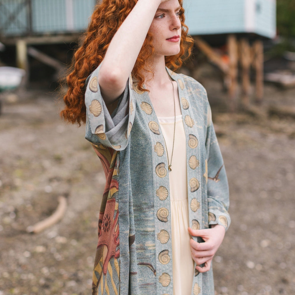 
                  
                    Lightweight duster featuring antique sunrise sky, mermaid, shell, and soaring birds artwork, shown on model at the beach – Market of Stars
                  
                