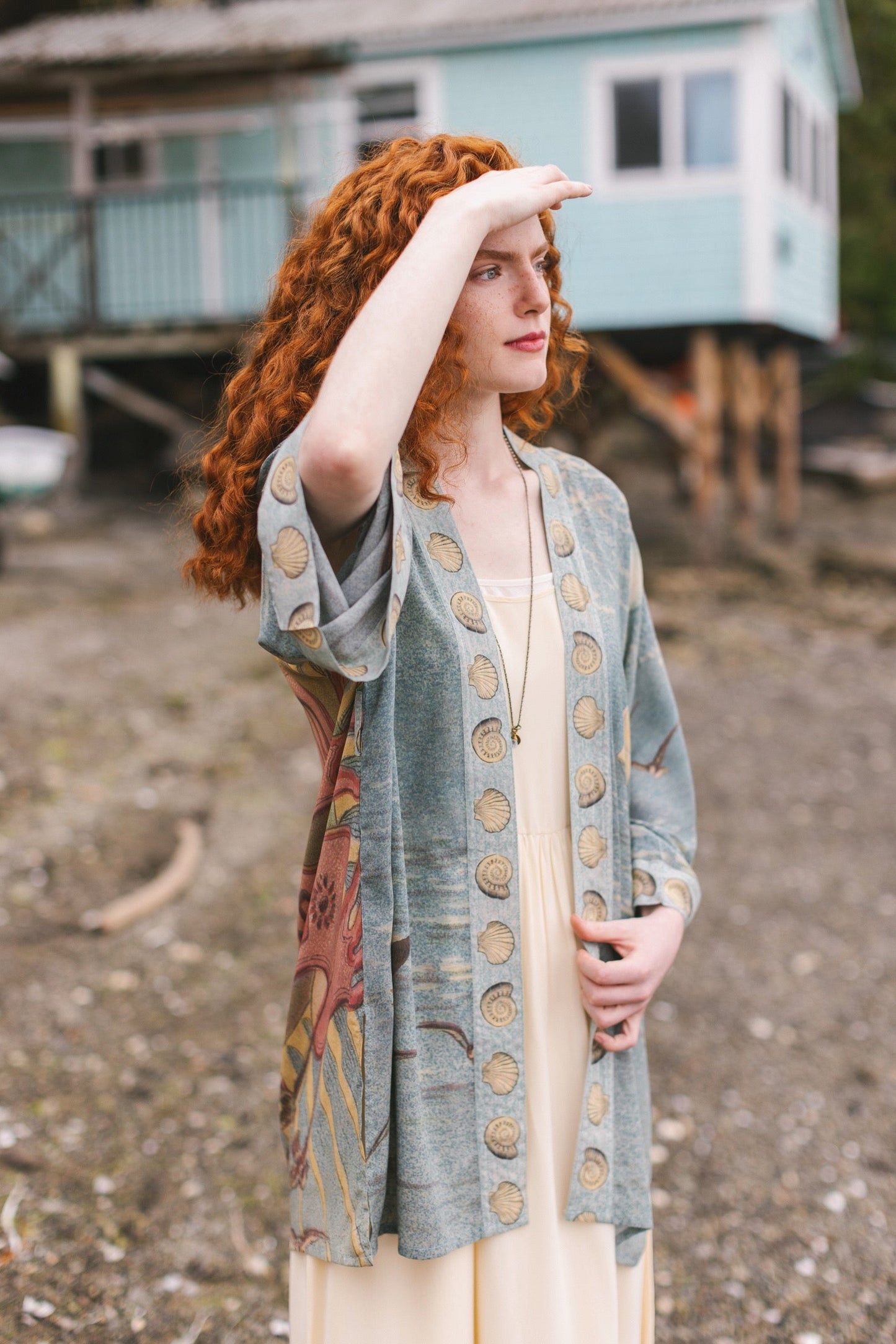 Lightweight duster featuring antique sunrise sky, mermaid, shell, and soaring birds artwork, shown on model at the beach – Market of Stars
