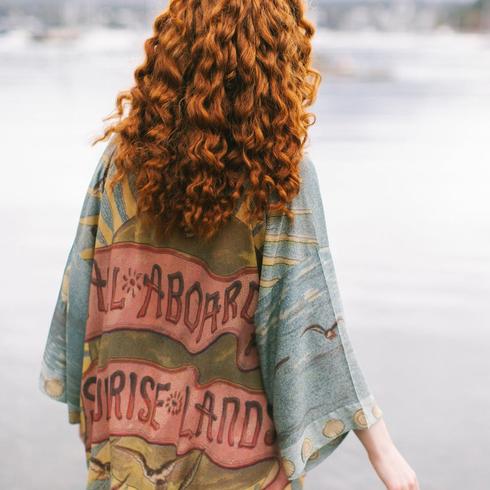 
                  
                    Lightweight duster featuring antique sunrise sky, mermaid, shell, and soaring birds artwork, shown on model at the beach – Market of Stars
                  
                