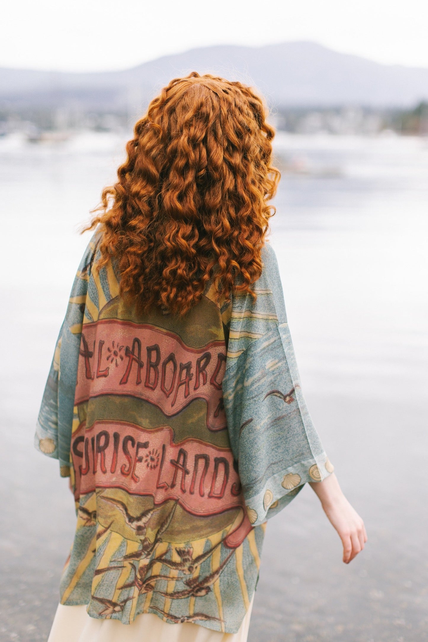 Lightweight duster featuring antique sunrise sky, mermaid, shell, and soaring birds artwork, shown on model at the beach – Market of Stars