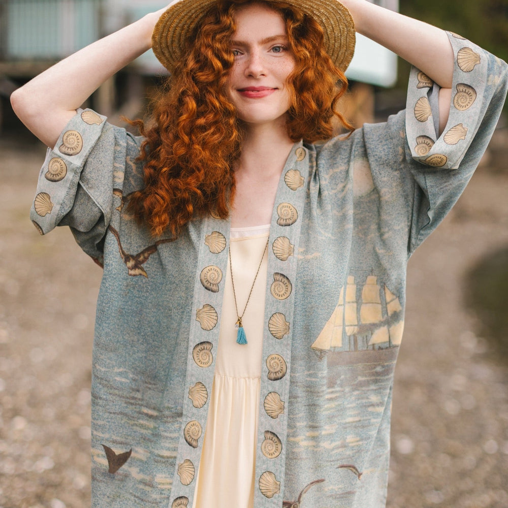 
                  
                    Lightweight duster featuring antique sunrise sky, mermaid, shell, and soaring birds artwork, shown on model at the beach – Market of Stars
                  
                