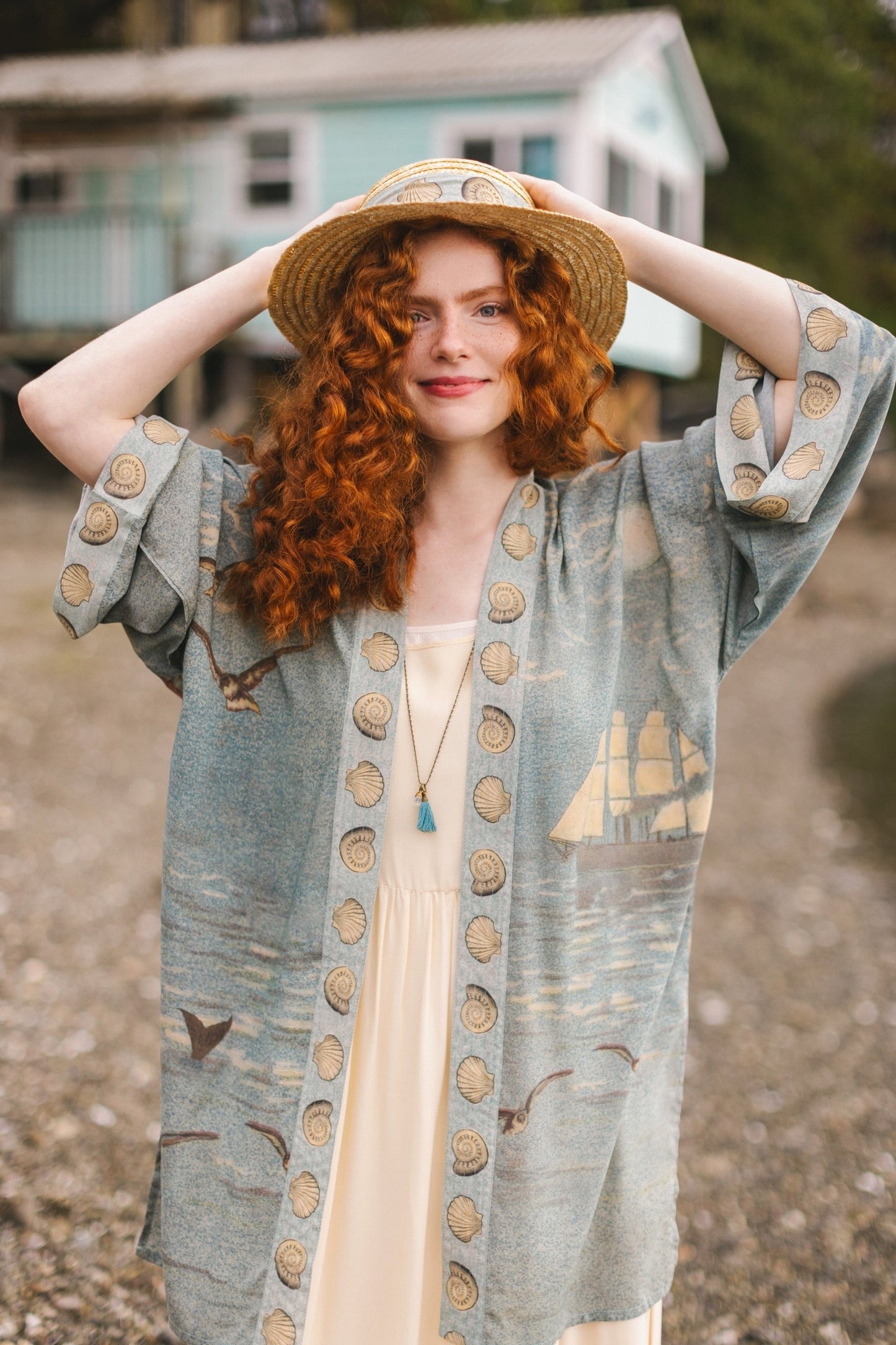 Lightweight duster featuring antique sunrise sky, mermaid, shell, and soaring birds artwork, shown on model at the beach – Market of Stars