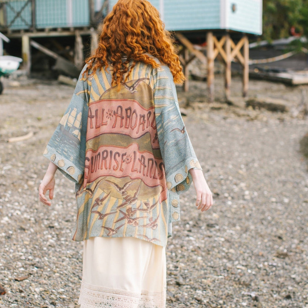 
                  
                    Lightweight duster featuring antique sunrise sky, mermaid, shell, and soaring birds artwork, shown on model at the beach – Market of Stars
                  
                
