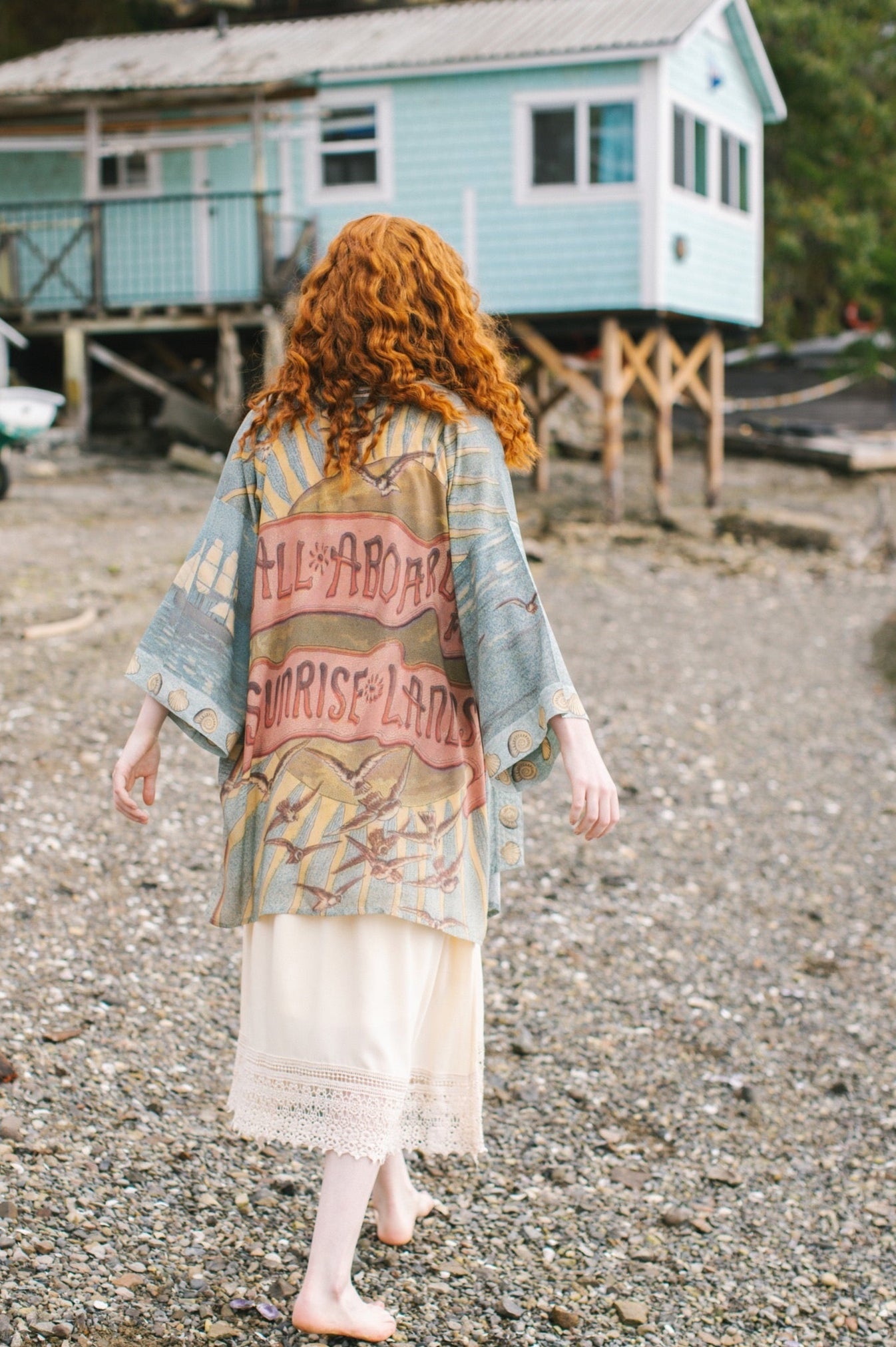 Lightweight duster featuring antique sunrise sky, mermaid, shell, and soaring birds artwork, shown on model at the beach – Market of Stars