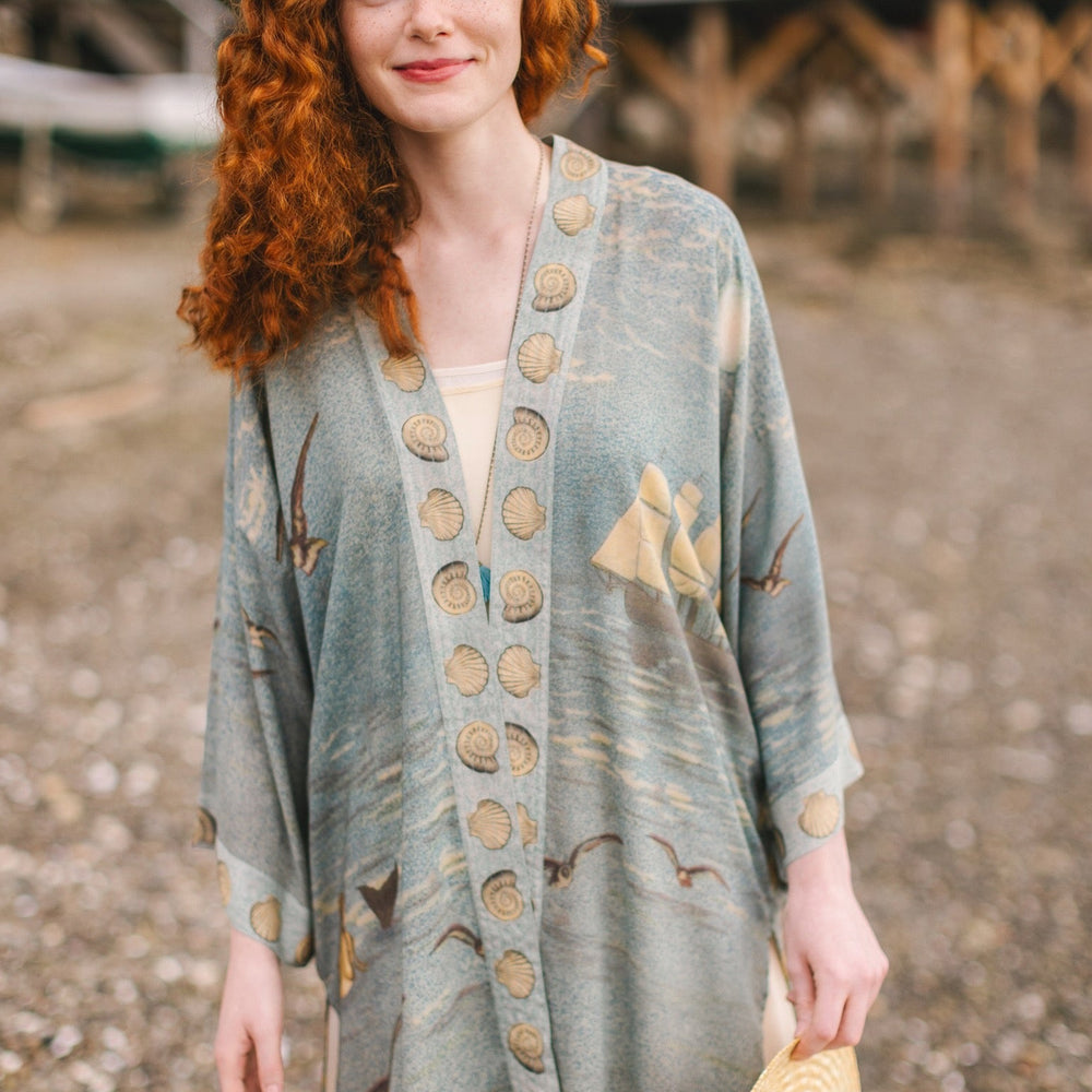 
                  
                    Lightweight duster featuring antique sunrise sky, mermaid, shell, and soaring birds artwork, shown on model at the beach – Market of Stars
                  
                
