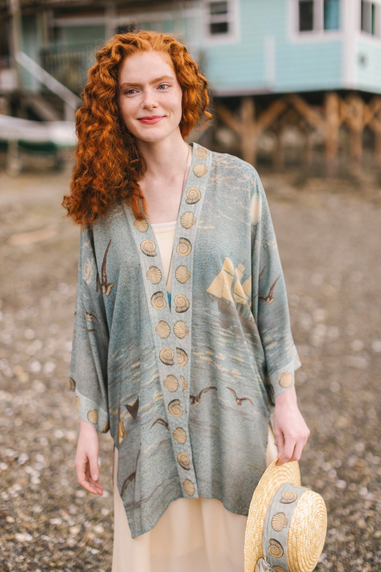 Lightweight duster featuring antique sunrise sky, mermaid, shell, and soaring birds artwork, shown on model at the beach – Market of Stars