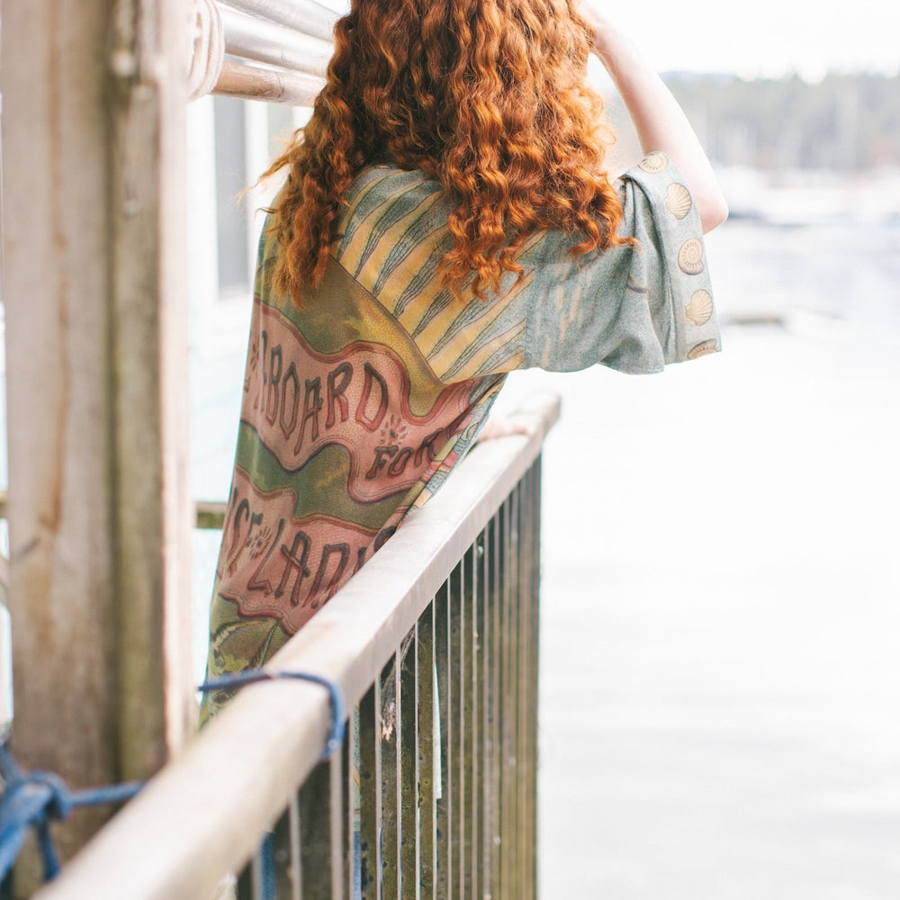 
                  
                    Lightweight duster featuring antique sunrise sky, mermaid, shell, and soaring birds artwork, shown on model at the beach – Market of Stars
                  
                