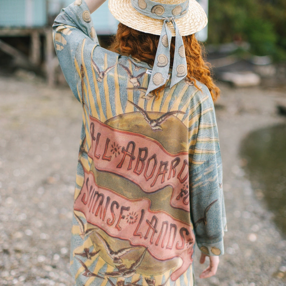 
                  
                    Lightweight duster featuring antique sunrise sky, mermaid, shell, and soaring birds artwork, shown on model at the beach – Market of Stars
                  
                