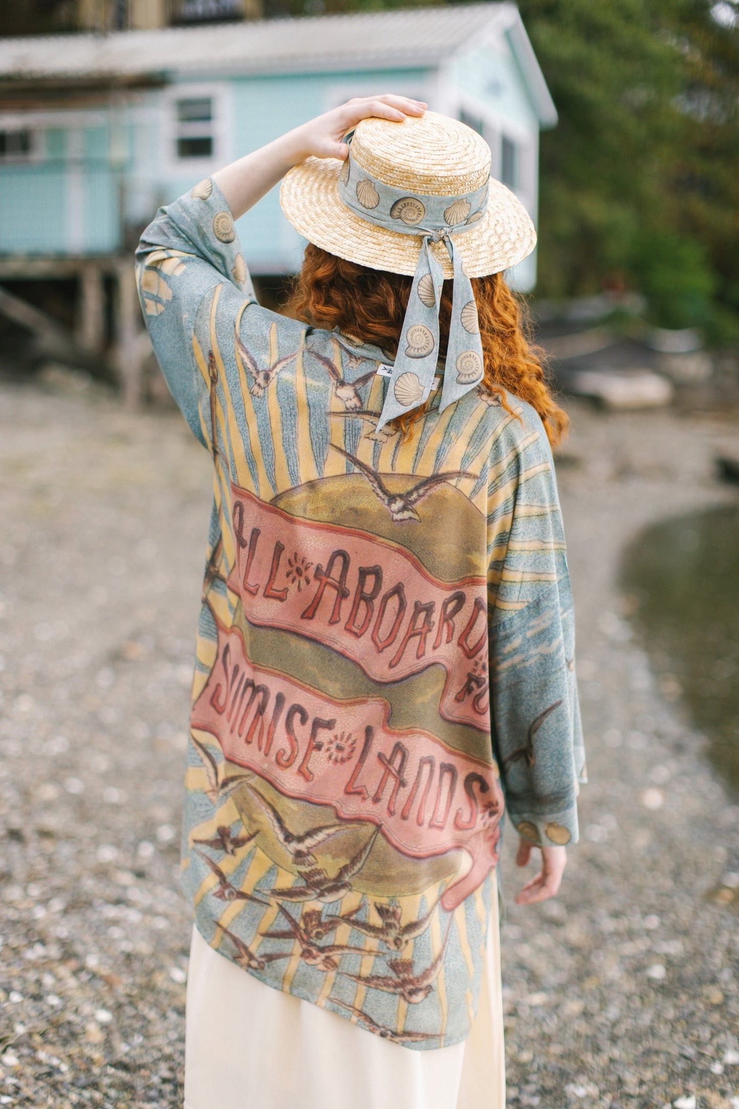 Lightweight duster featuring antique sunrise sky, mermaid, shell, and soaring birds artwork, shown on model at the beach – Market of Stars