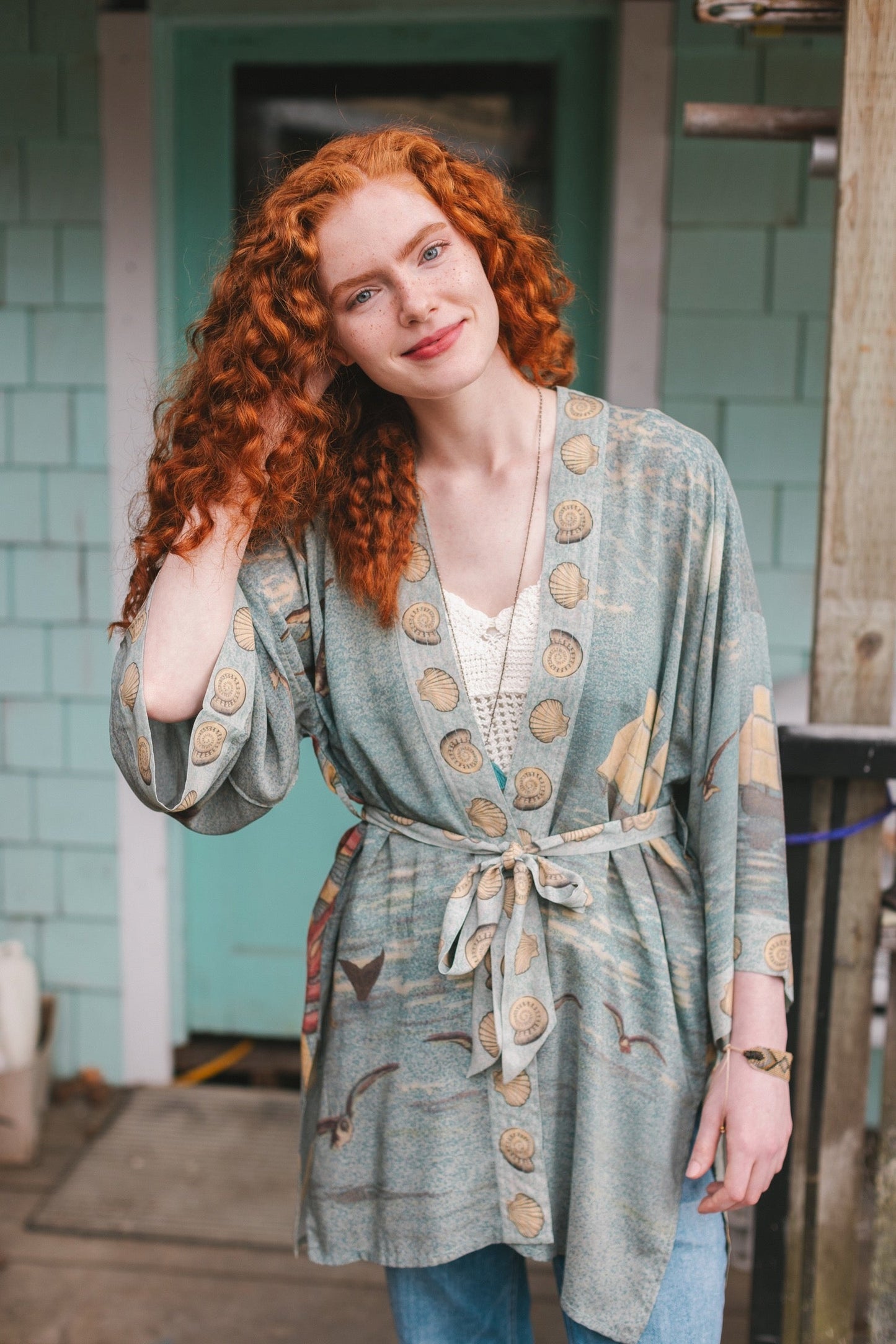 Lightweight duster featuring antique sunrise sky, mermaid, shell, and soaring birds artwork, shown on model at the beach – Market of Stars